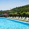 Piscina con scivolo blu, sdraio bianche su prato, colline sullo sfondo.
