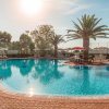 Piscina azzurra con palme e ombrelloni sotto il sole.
