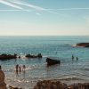 Persone in mare vicino a scogli, cielo limpido.