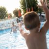 Bambino gioca in piscina spruzzando acqua con amico.