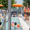 Lezione in piscina con istruttrici sotto ombrelloni arancioni.