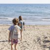 Due bambini camminano verso il mare su una spiaggia.