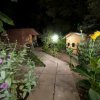 Sentiero illuminato di notte tra bungalow e piante fiorite.