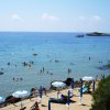 Spiaggia affollata con mare calmo e ombrelloni.