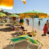 Spiaggia con ombrelloni verdi e gialli. Persone godono del sole e del mare.
