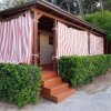 Casetta in legno con tende a strisce, circondata da cespugli.