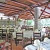 Ampio ristorante all'aperto con tavoli apparecchiati e sedie di legno sotto un tetto rustico.