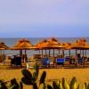 Spiaggia con ombrelloni di paglia, lettini e mare sullo sfondo.