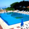 Una grande piscina rettangolare con sdraio e ombrelloni blu intorno, vista sul mare.