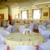Tavoli rotondi apparecchiati in una sala banchetti elegante con sedie coperte da fodere bianche.