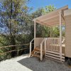 Veranda in legno affacciata su un giardino con alberi, sotto un cielo blu.