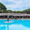 Piscina azzurra con statua di surfista, tetto di paglia e alberi sullo sfondo.